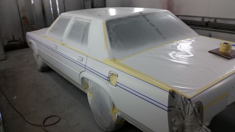 1991 Ford LTD Crown Victoria - A white sedan is covered in plastic and tape, likely in a paint booth, with blue pinstripes visible.