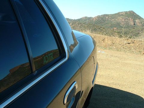 1998 Ford Crown Victoria - Rear quarter window and door of a dark green sedan parked on a dirt overlook with hills behind.