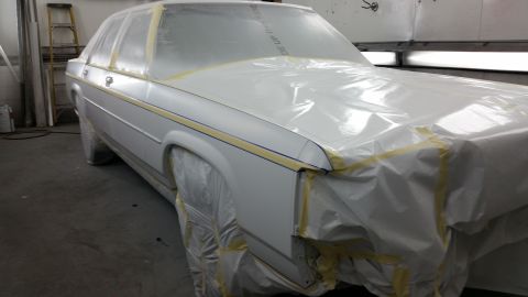 1991 Ford LTD Crown Victoria - A white 1991 Ford Crown Victoria LTD is prepped for painting, covered in protective plastic and tape inside a paint booth.
