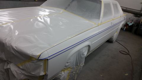 1991 Ford LTD Crown Victoria - A white sedan is covered in protective plastic and tape, ready for a paint job in a workshop.