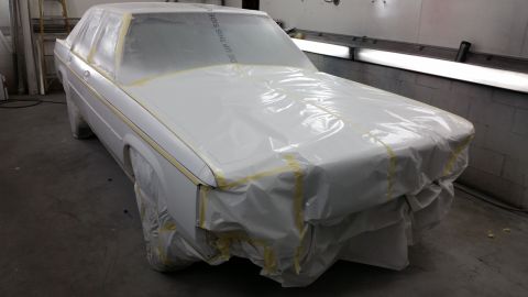 1991 Ford LTD Crown Victoria - A car is prepped for painting, with plastic sheeting and tape covering most of its body.