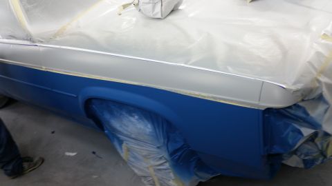 1991 Ford LTD Crown Victoria - A car's side panel is covered in plastic sheeting as it undergoes a paint job, revealing blue and silver colors.