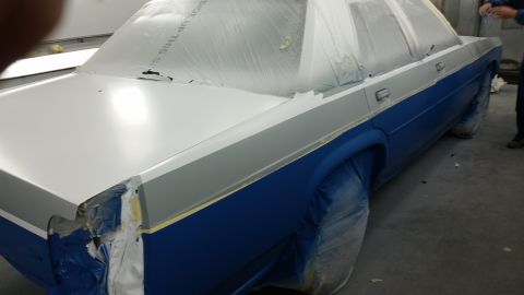 1991 Ford LTD Crown Victoria - A car is being prepped for painting in a workshop, with protective coverings on its wheels and windows.