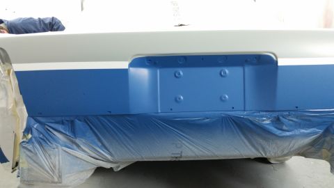 1991 Ford LTD Crown Victoria - The rear bumper area of a car is being painted blue, with a white stripe above it, and is covered in protective plastic.