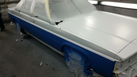 1991 Ford LTD Crown Victoria - A car is being prepped for painting in a booth, with protective coverings on its windows and wheels.