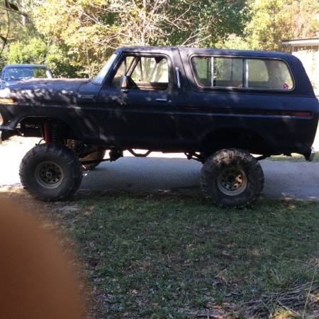 1979 Ford Bronco - Side profile of a modified Ford Bronco, likely from the late 1970s, with significant suspension lift and oversized tires.