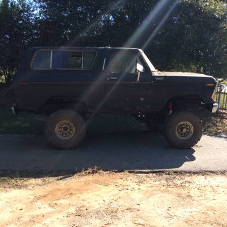 1979 Ford Bronco - Side view of a dark-colored SUV with large tires and lifted suspension.