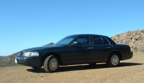 1998 Ford Crown Victoria - Side profile of a dark green Ford Crown Victoria sedan parked on a dirt overlook with rocks behind.