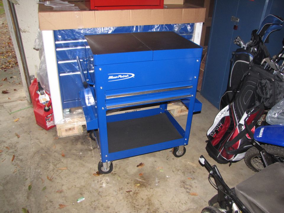 Blue Blue-Point tool cart next to golf bags, a red gas can, and a blue cabinet
