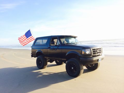 1992 Ford Bronco - A black 1992 Ford Bronco flies an American flag while parked on a sandy beach.
