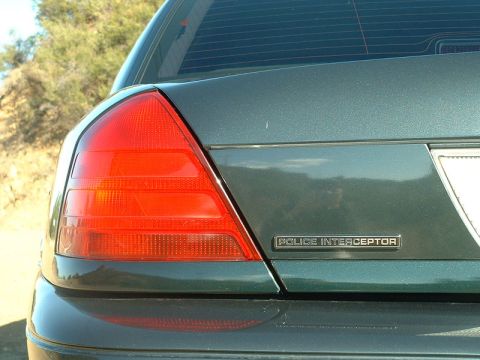 1998 Ford Crown Victoria - Close-up of the rear taillight and Police Interceptor trunk badge on a dark green Ford sedan.