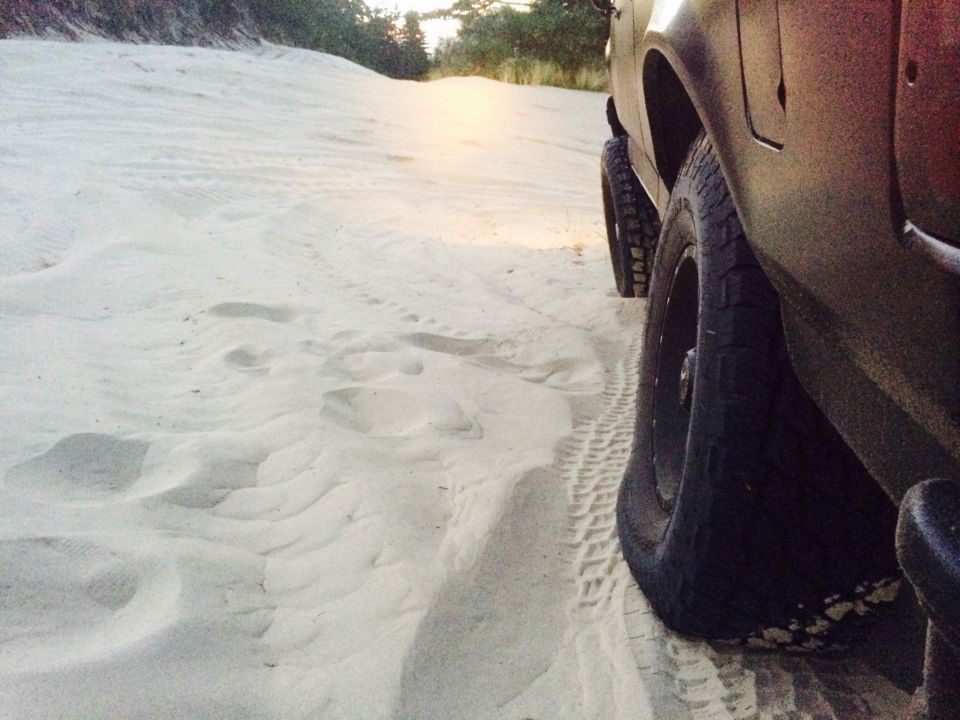 Dark-colored 1992 Ford Bronco side view on sand dunes, showing front tire and part of rear tire