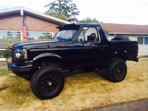 1992 Ford Bronco - Black 1992 Ford Bronco parked in front of a brick house on a sunny day.
