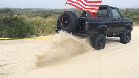 1992 Ford Bronco - This 1992 Ford Bronco is shown driving on a sandy terrain with an American flag attached.