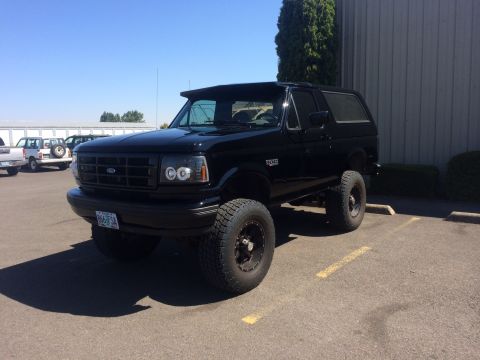 1992 Ford Bronco - This black Ford Bronco is parked in a lot with other vehicles visible in the background.