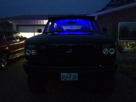1992 Ford Bronco - A 1992 Ford Bronco is parked in front of a garage at dusk, with blue lights illuminating the interior.