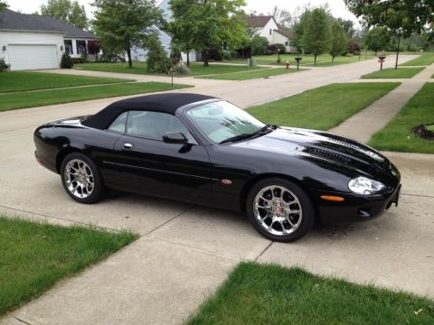 1998 Ford Crown Victoria - A black convertible sports car is parked on a driveway in front of a house.