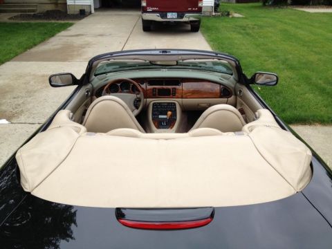 1998 Ford Crown Victoria - The interior of a black convertible is shown, tan leather seats and wood accents on the dashboard and center console. A red pickup truck is…
