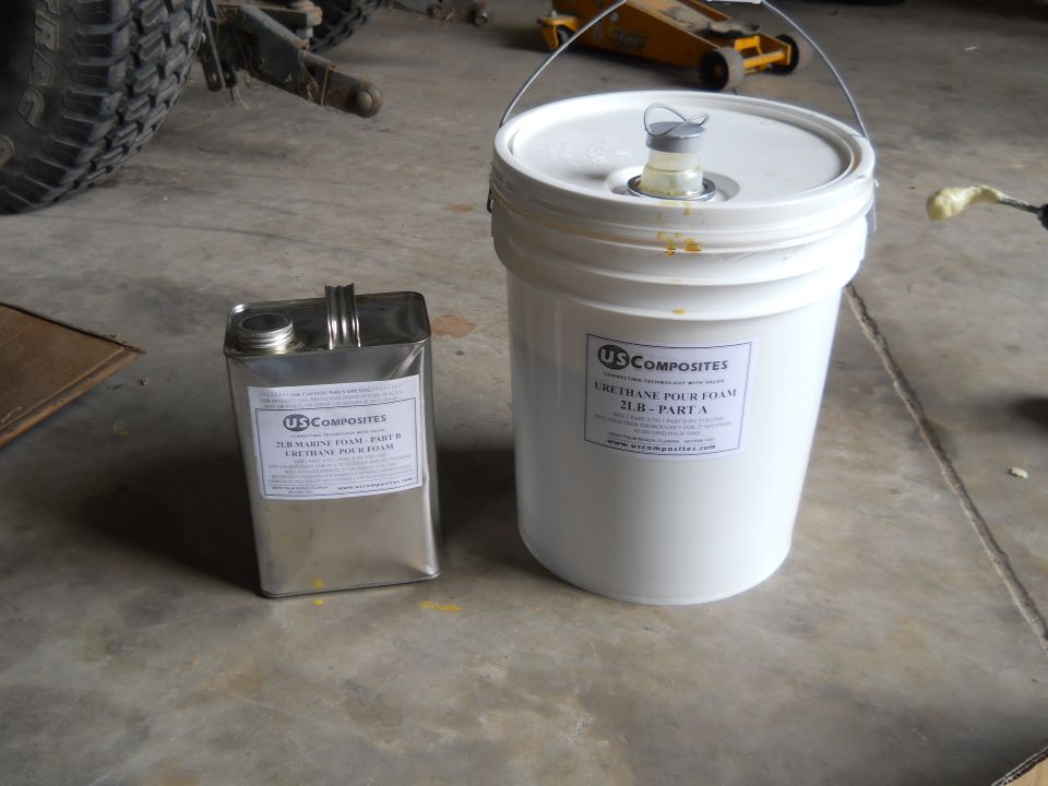 Two containers of US Composites urethane pour foam, one metal can and one white bucket, on a concrete floor