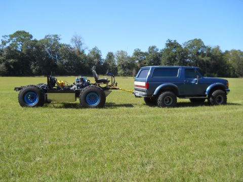 1992 Ford Bronco - A blue Ford Bronco tows a custom-built chassis with a seat and engine across a grassy field.