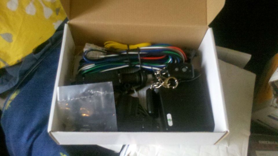 Car alarm system components including a black box, wiring harness, and key fob in an open cardboard box