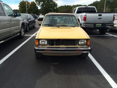 1983 Volkswagen Rabbit - Front view of a yellow 1983 Volkswagen Rabbit parked in a lot with other vehicles.