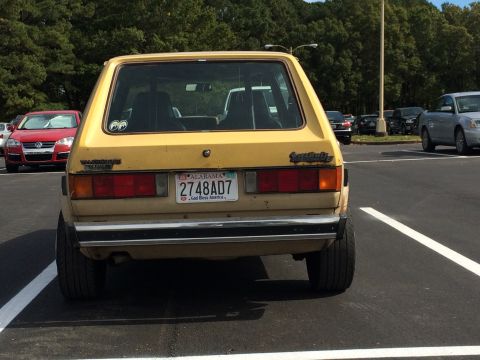 1983 Volkswagen Rabbit - A yellow 1983 Volkswagen Rabbit is seen from the rear in a parking lot with other vehicles around.