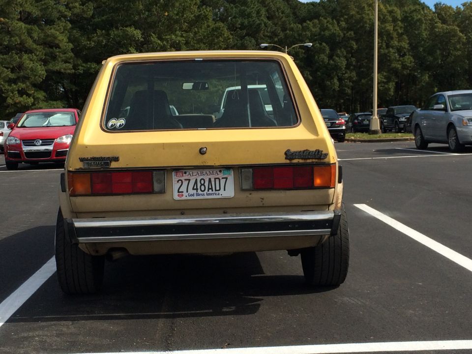 Yellow 1983 Volkswagen Rabbit parked in a lot, rear view. The car has a chrome bumper and Alabama license plate