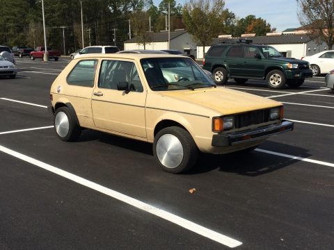 1983 Volkswagen Rabbit - Tan 1983 Volkswagen Rabbit with large, flat hubcaps is parked in a lot.