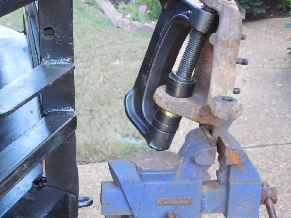 Ball joint press tool on rusty knuckle held in blue Kobalt vise outdoors
