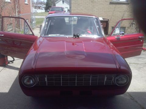 1960 Ford Falcon - Front view of a red 1960 Ford Falcon, doors open. A second vehicle is visible in the background.