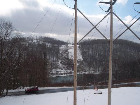 1990 Ford Bronco - A red SUV travels down a road during a winter snowfall, with power lines overhead and a river nearby.