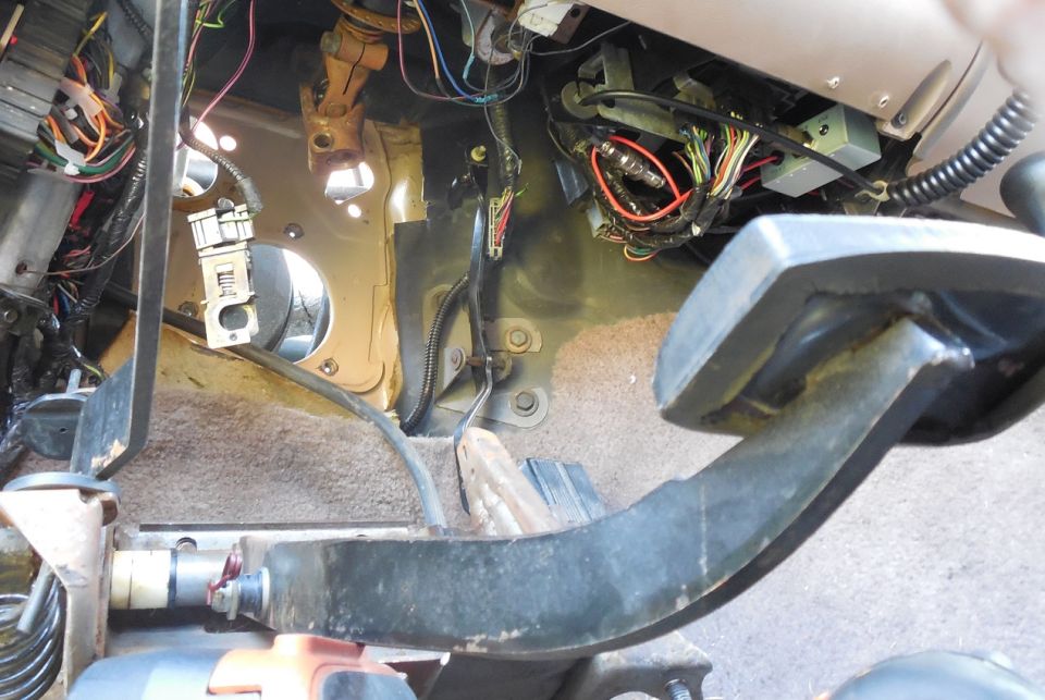 Under-dash view showing pedal arm, exposed wiring harnesses, and firewall of an old truck interior.
