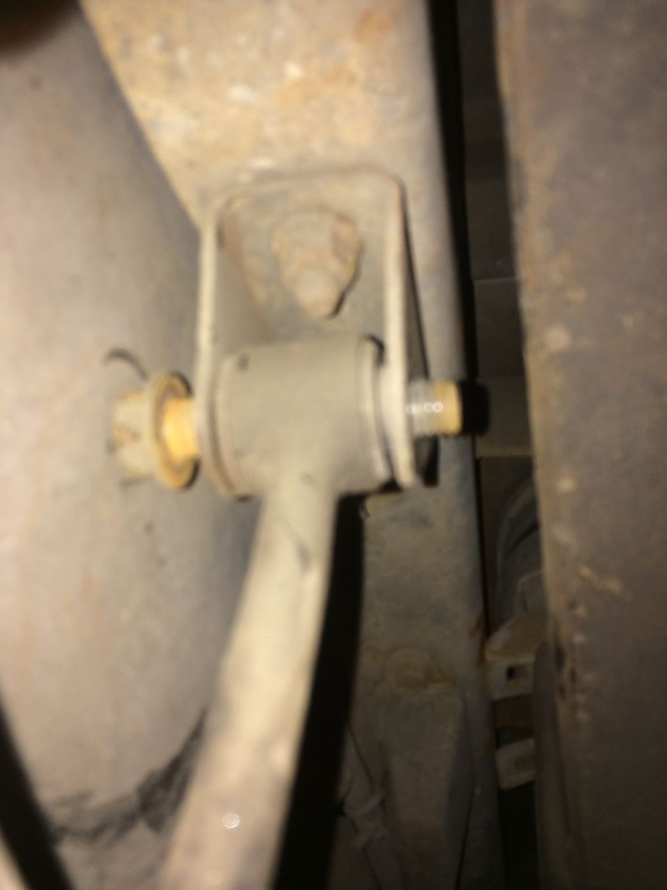 Sway bar link with yellow bushings attached to a rusty bracket
