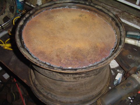 1993 Ford Bronco - A heavily rusted wheel rim sits on a workbench, showing signs of modification.