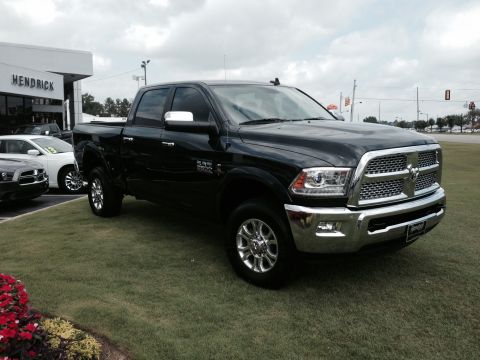 1989 Ford Bronco - A black Ram pickup truck is parked on a grassy lot in front of a dealership building.