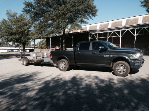 1989 Ford Bronco - A dark gray pickup truck tows a trailer loaded with materials, parked in front of a building.