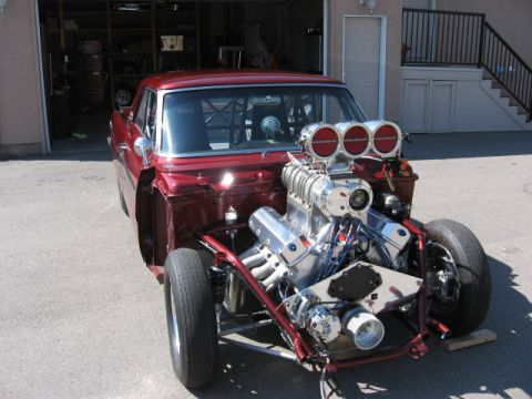 1965 Ford Fairlane - A custom 1965 Ford Fairlane drag car is shown with its hood removed, revealing a powerful engine and supercharger.