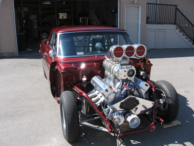 Red 1965 Ford Fairlane drag car with a large supercharger and exposed engine, viewed from the front