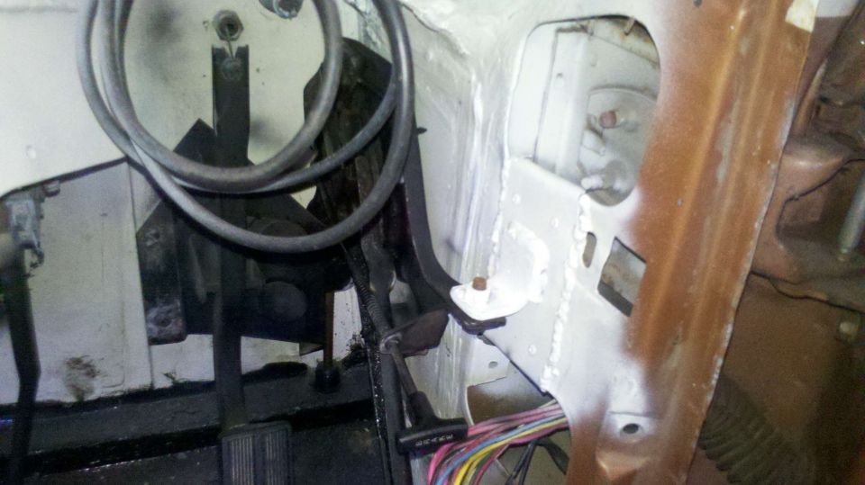 Close-up of vehicle's firewall area with brake and clutch pedals visible, along with wiring harness