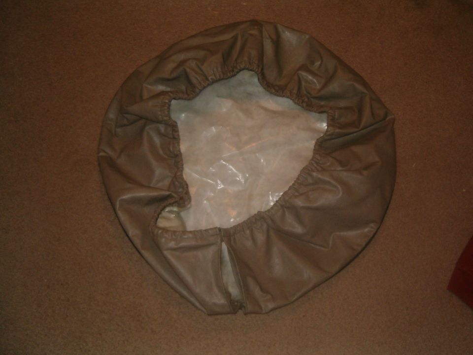 Tan vinyl spare tire cover laid inside-up on brown carpet showing elastic edge