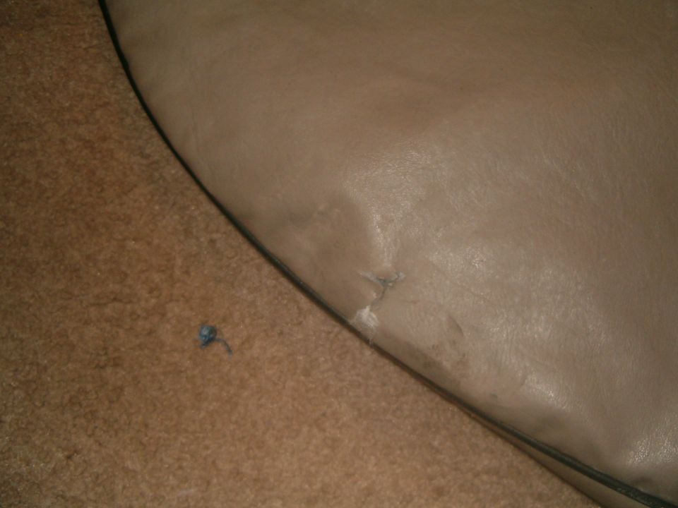 Close-up of torn tan interior upholstery with carpeted floor visible