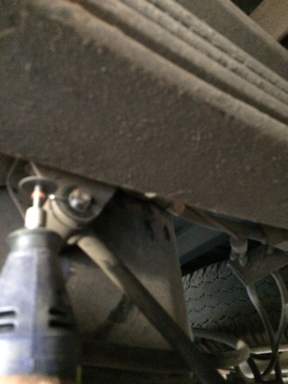 Close-up of a truck's rear leaf springs and suspension components. A tool is visible near a bolt