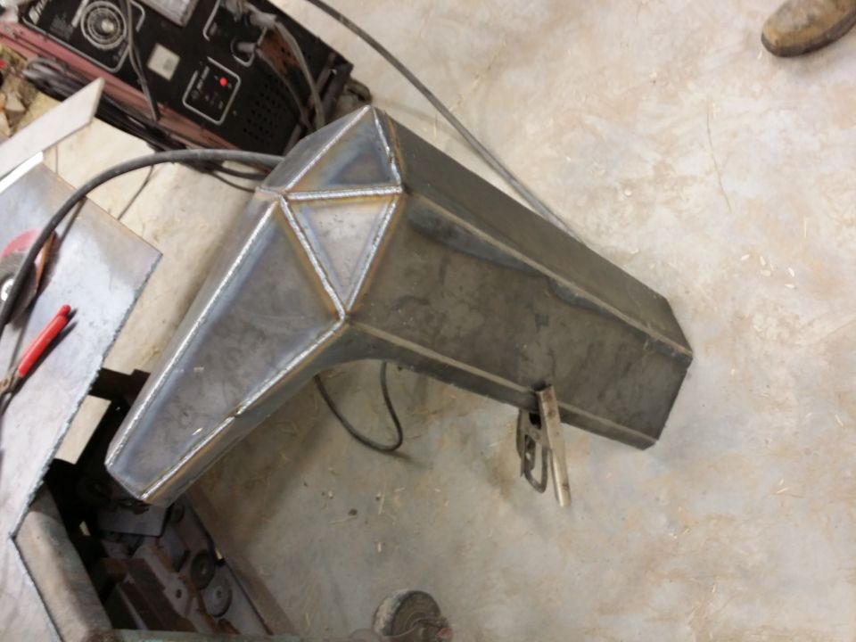 Custom metal bumper being fabricated, showing welded seams and angular design. A welding machine is visible in the background