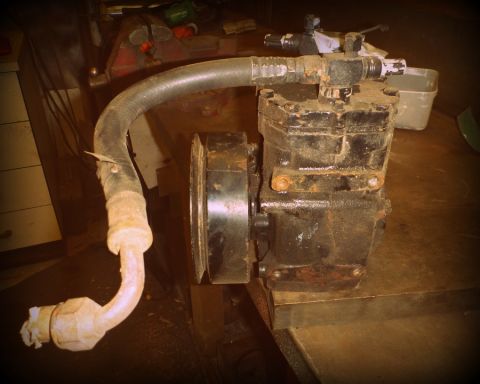 1964 Mercury Monterey - A close-up view of a black air conditioning compressor with attached hoses, resting on a wooden surface.