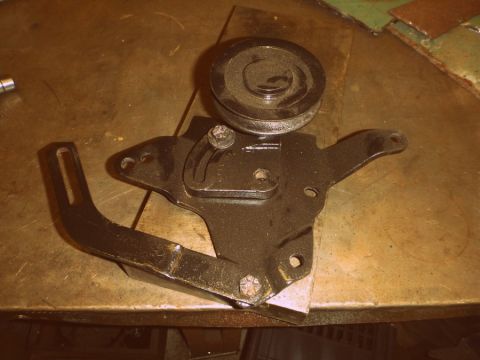 1964 Mercury Monterey - A close-up view of a pulley bracket with a roller, likely a car part, on a metal surface.