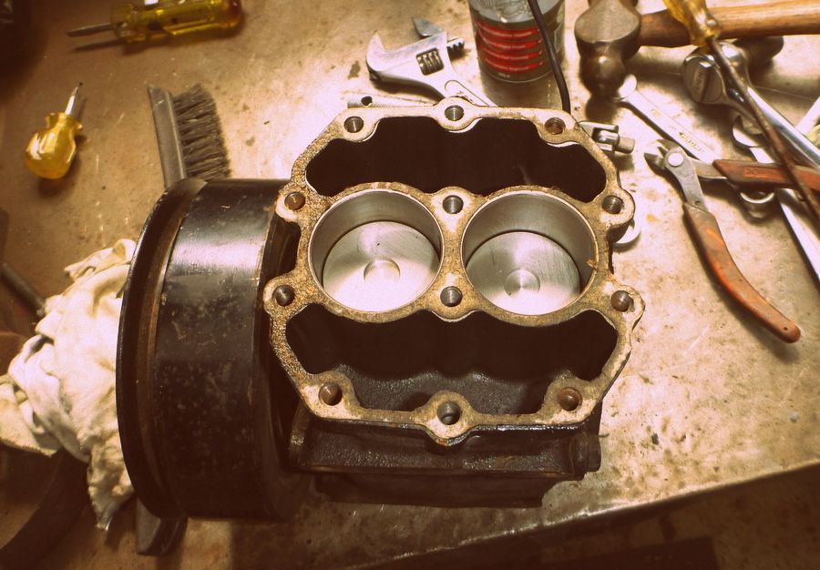 Engine block with two cylinders and pistons visible, surrounded by tools