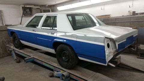 1991 Ford LTD Crown Victoria - A two-tone blue and silver sedan is shown on a lift in a workshop, with its front end partially dismantled.