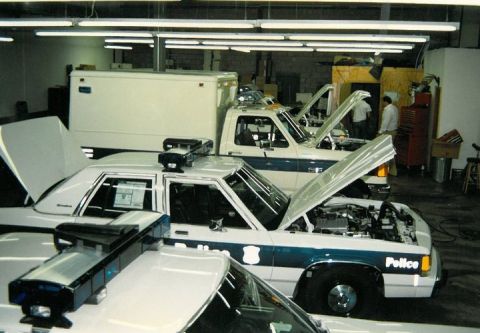1991 Ford LTD Crown Victoria - Several police vehicles are parked in a garage with their hoods open, suggesting maintenance or inspection.