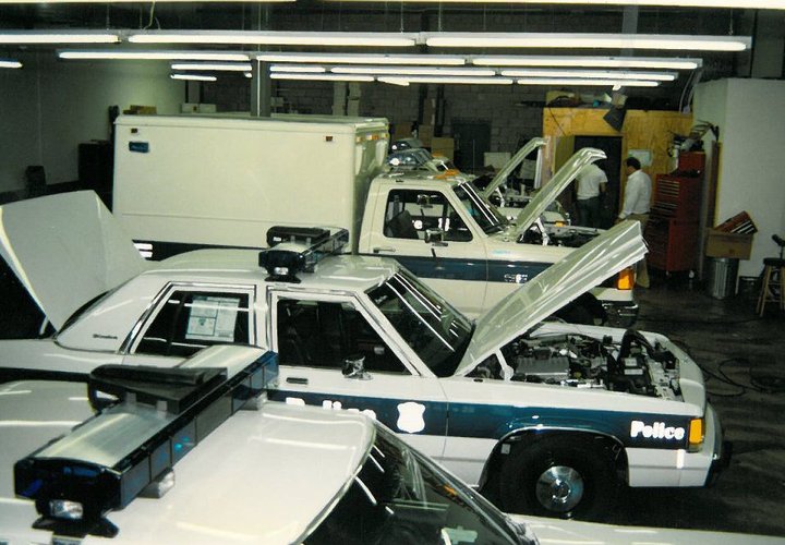 Police Crown Victoria with hood open, showing engine. White and blue paint, police light bar on roof